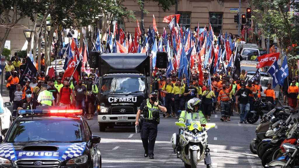 A crowd of hundreds of unionists with flags from the CMFEU marching down a street in Brisbane