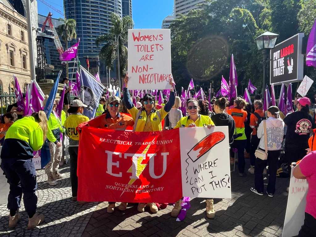 A crowd of women construction workers holding signs and banners demanding better women's bathroom facilities. One sign reads "Women's Toilets Are Non-Negotiable," while another features a drawing of a tampon with the words "Where can I put this?" The protesters are wearing high-visibility work clothing, and numerous union flags and banners from the ETU and CFMEU are visible in the background.